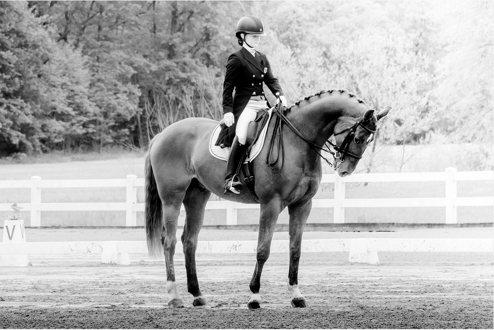 Black and white picture of a person wearing riding gear riding a horse
